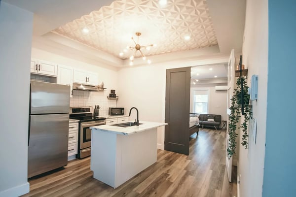 Modern kitchen with white cabinetry, stainless steel appliances, central island, textured ceiling, and open-plan layout connecting to living area.